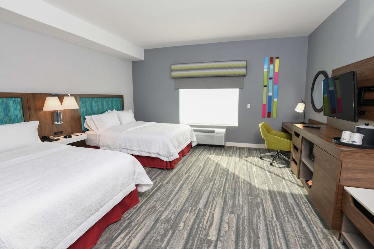 A hotel room with two beds, a desk, a chair, a TV, and a window.