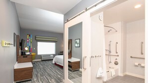 Ein modernes Hotelzimmer mit einem großen Bett, einem begehbaren Kleiderschrank, einem Badezimmer mit Dusche und Blick auf die Stadt.