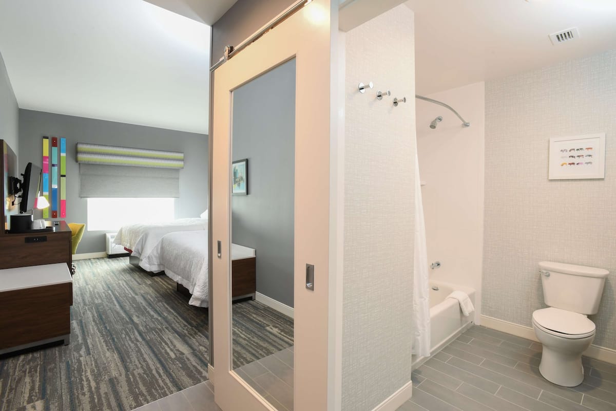 A modern hotel room with a large bed, a desk, a shower, and a toilet.