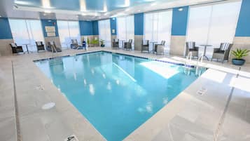 An indoor swimming pool with clear water, surrounded by lounge chairs and tables.
