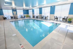 Una piscina interior con agua cristalina, rodeada de sillas y mesas de descanso.