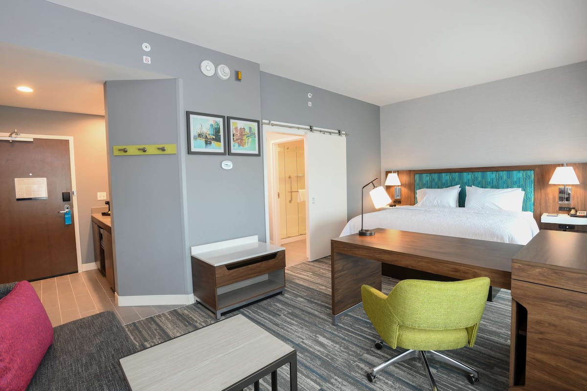 A hotel room with a bed, desk, chair, and a bathroom visible through an open door.