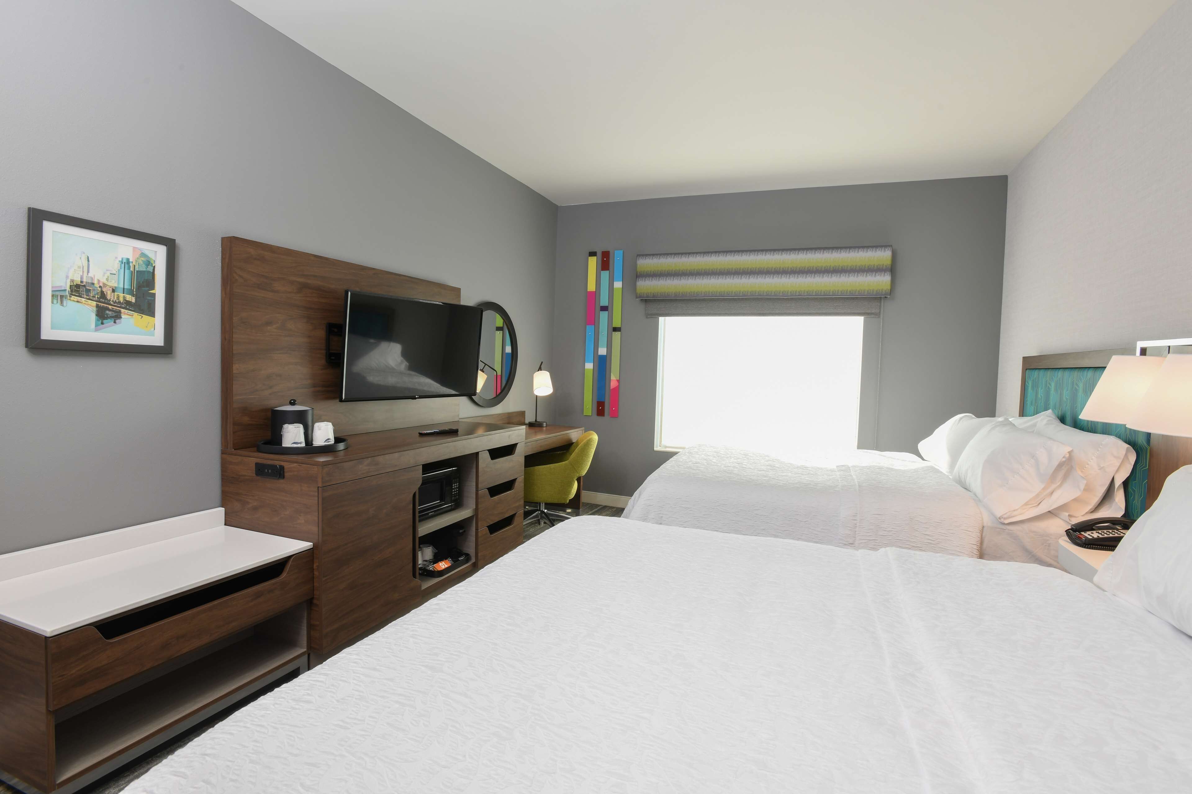 Habitación de hotel con cama, escritorio con televisor, una silla, ventana con vistas y mesita de noche.