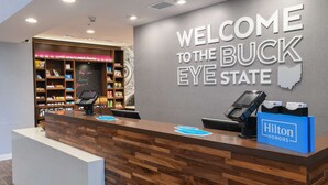 Ein Empfangsschalter mit einem Schild, auf dem 'Welcome to the Buck Eye State' steht, einem blauen Hilton Honors-Schild und einem Selbstbedienungs-Check-in-Automaten.
