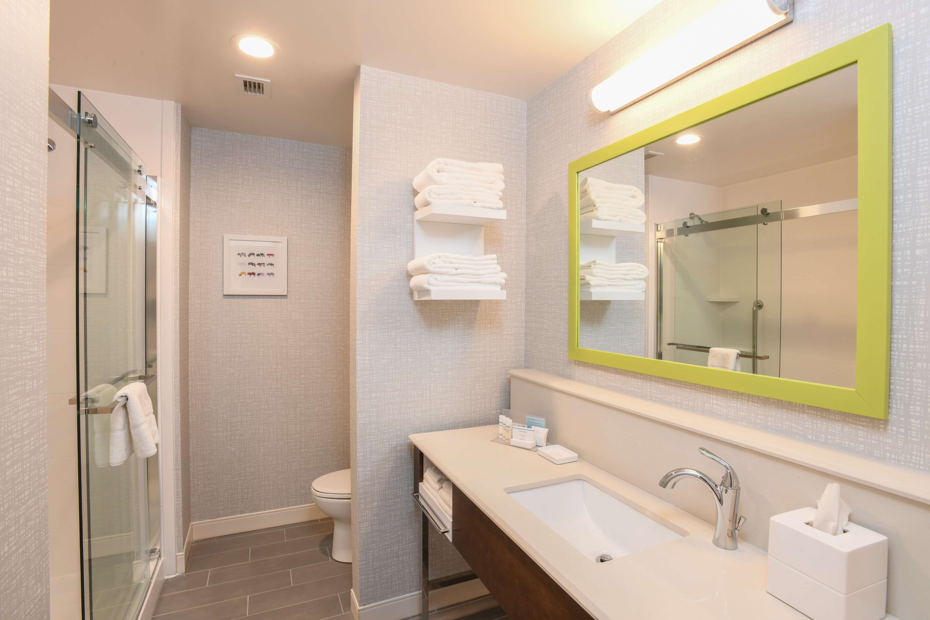 A modern bathroom with a glass shower, a sink with a mirror, and neatly folded towels on a shelf.