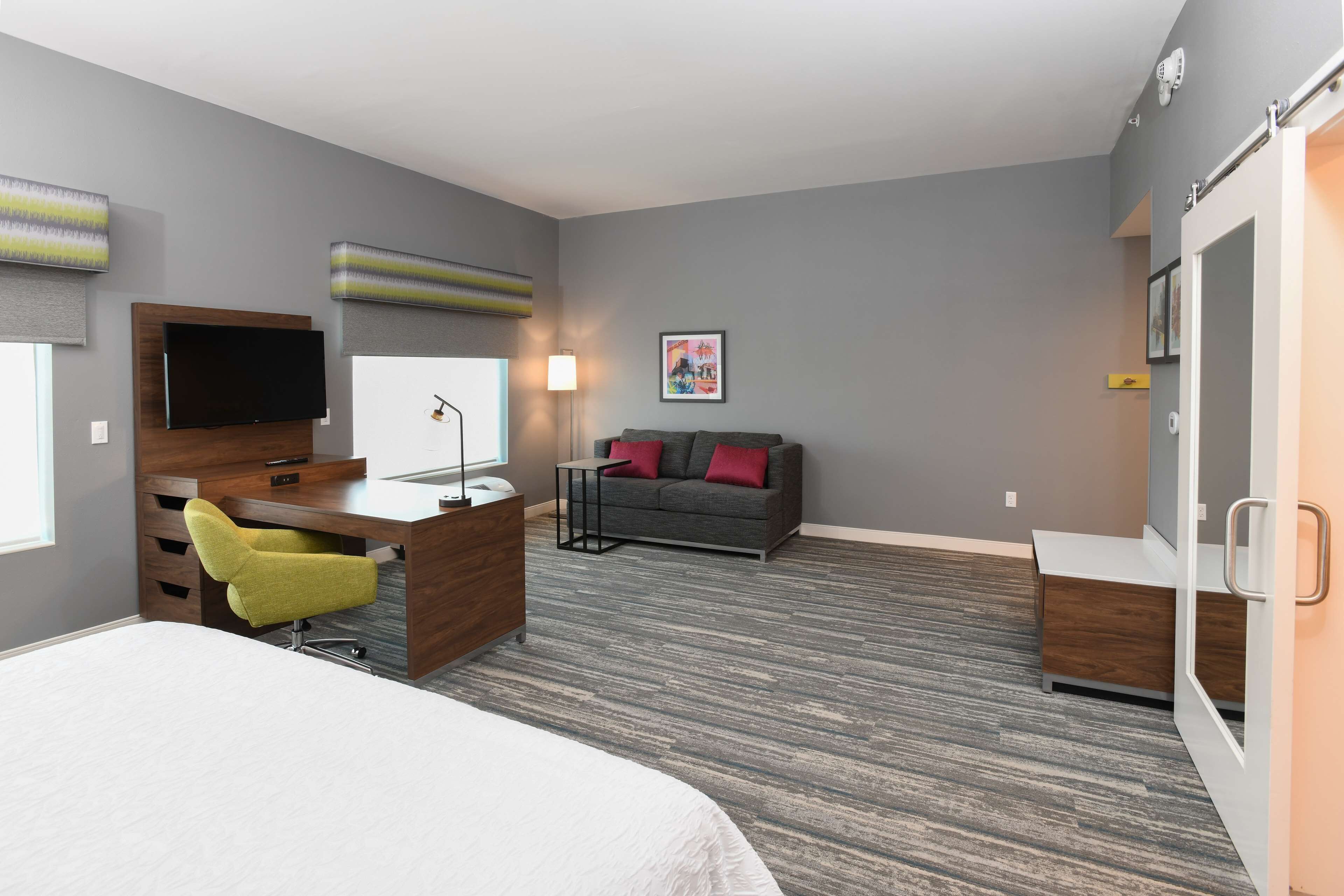 A modern hotel room with a bed, desk, chair, sofa, and a TV.