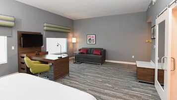 A modern hotel room with a bed, desk, chair, sofa, and a TV.
