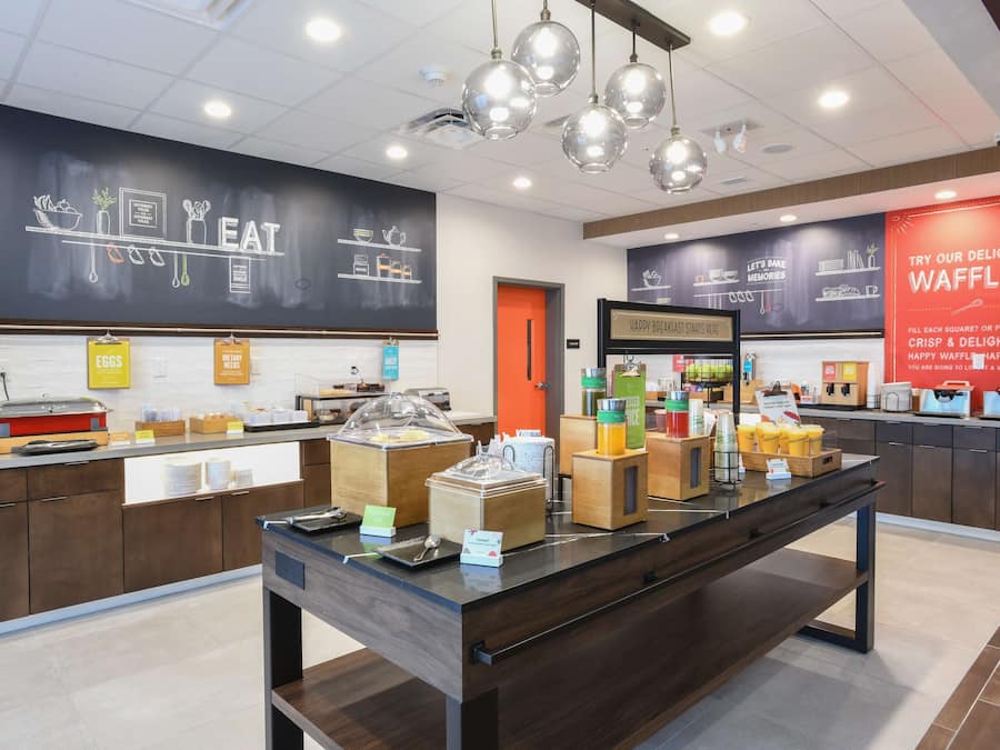A breakfast buffet area with various food stations, including a waffle station, and a chalkboard menu.