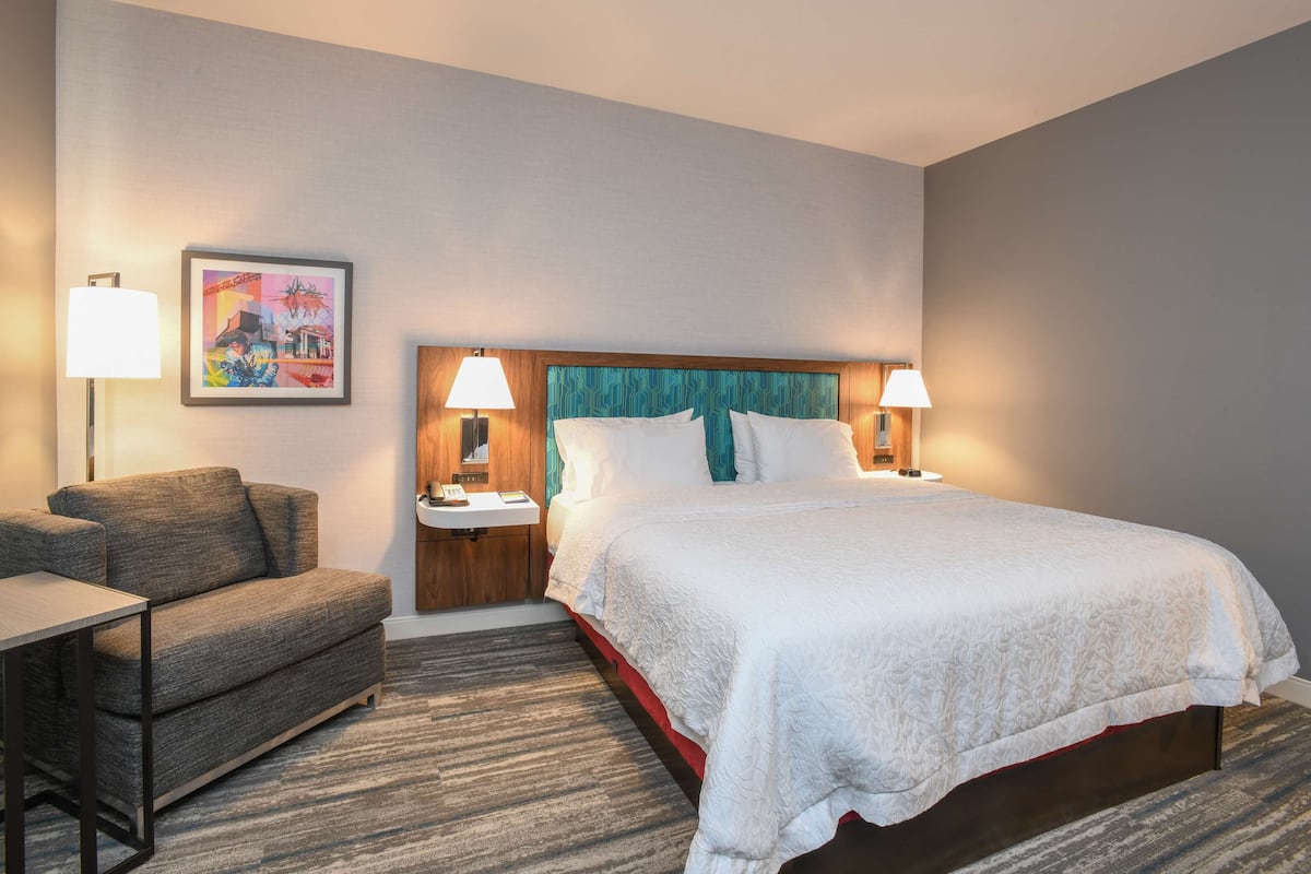 A hotel room with a bed, a sofa, a nightstand, and a lamp.