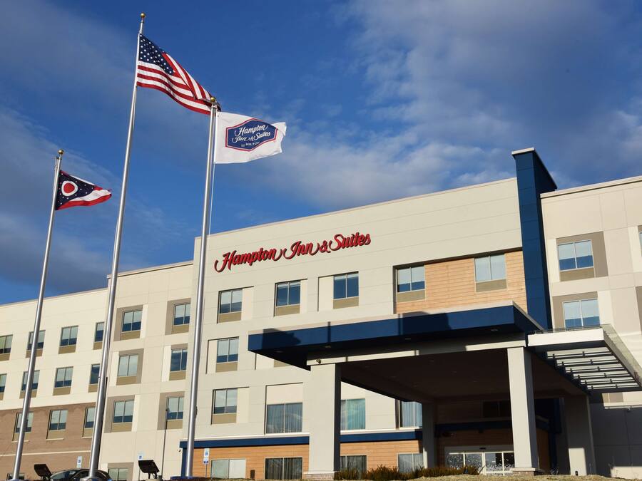 Een Hampton Inn & Suites hotel met een moderne gevel, meerdere ramen en een heldere lucht.