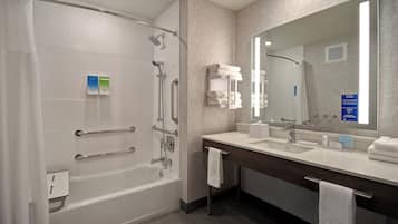 A modern bathroom with a walk-in shower, grab bars, a large mirror, and a vanity with a sink and towel rack.