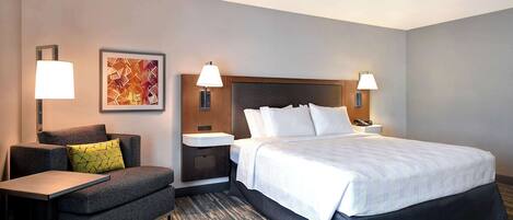 A hotel room with a large bed, a sofa, a small table, and two wall-mounted lamps.