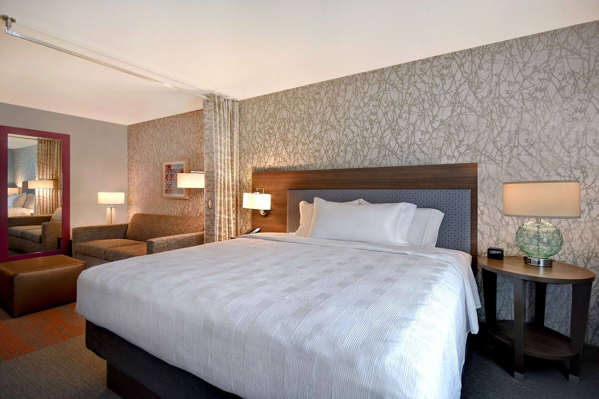 Hotelkamer met een groot bed, twee nachtkastjes, een stoel, een spiegel en een behang met patroon.