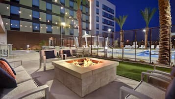 Un área de estar al aire libre con una chimenea, sillones de descanso y una piscina al fondo.