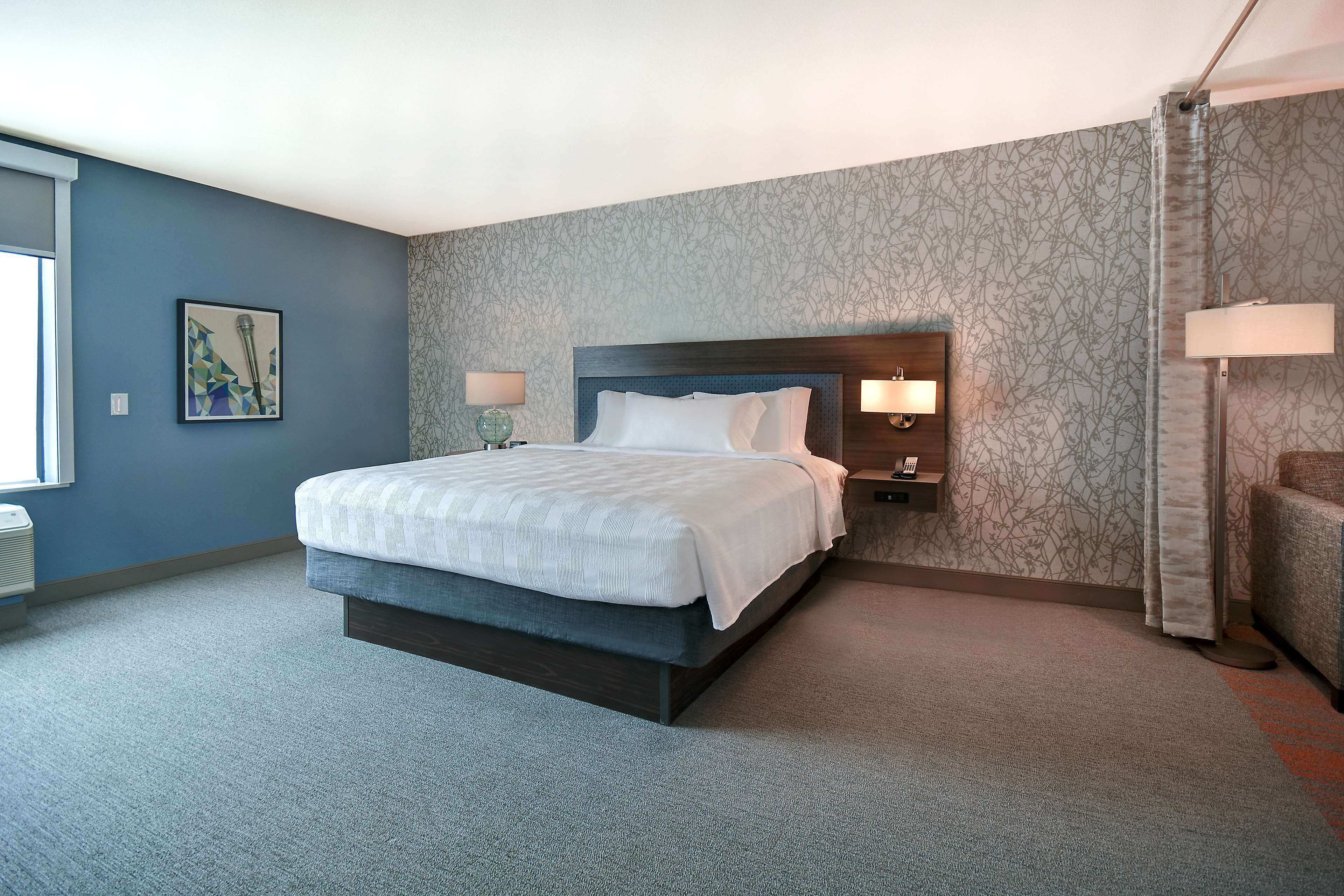 Ein modernes Hotelzimmer mit einem großen Bett, zwei Nachttischen mit Lampen, einem großen Fenster und einer Wand mit Muster.