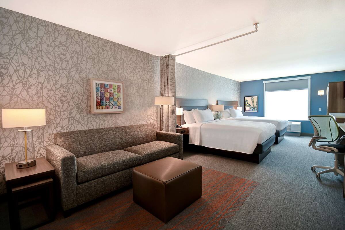 Hotelkamer met een bed, een slaapbank, een salontafel, een bureau met een stoel en een raam met gordijnen.