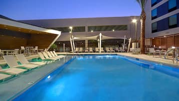 Une piscine entourée de chaises longues et de parasols, le tout bordé d’un bâtiment moderne doté de grandes fenêtres.