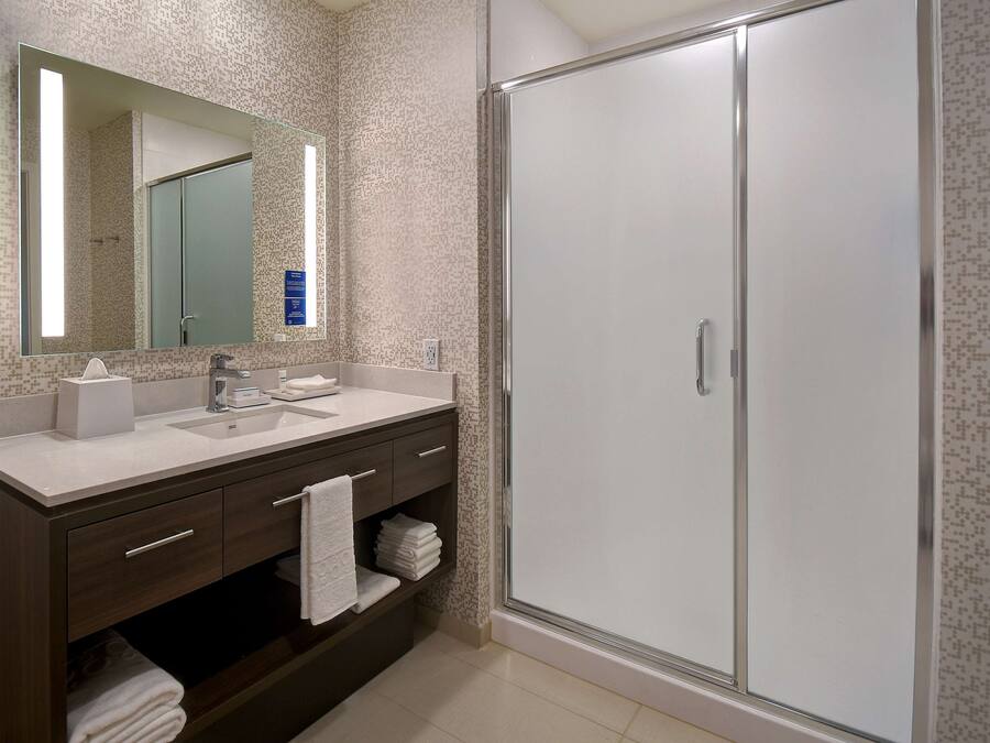 Een moderne badkamer met een grote spiegel, een wastafel, een badkamerkast met lades en een inloopdouche.
