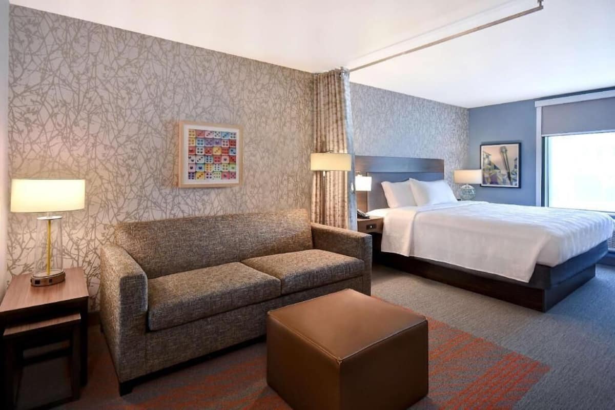Een hotelkamer met een bed, een slaapbank, een bijzettafeltje, een lamp en een decoratief wandobject.