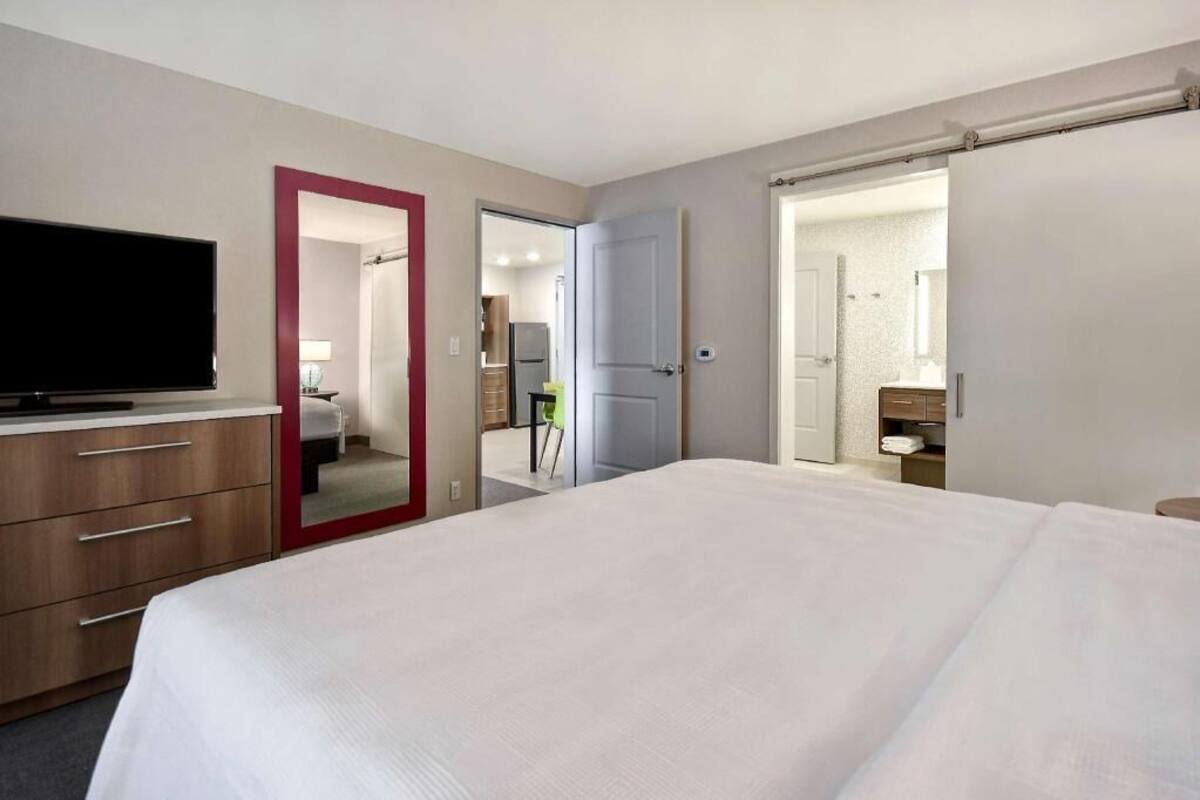 Een hotelkamer met een bed, een televisie, een bureau met lades, een spiegel en een deur naar een badkamer.