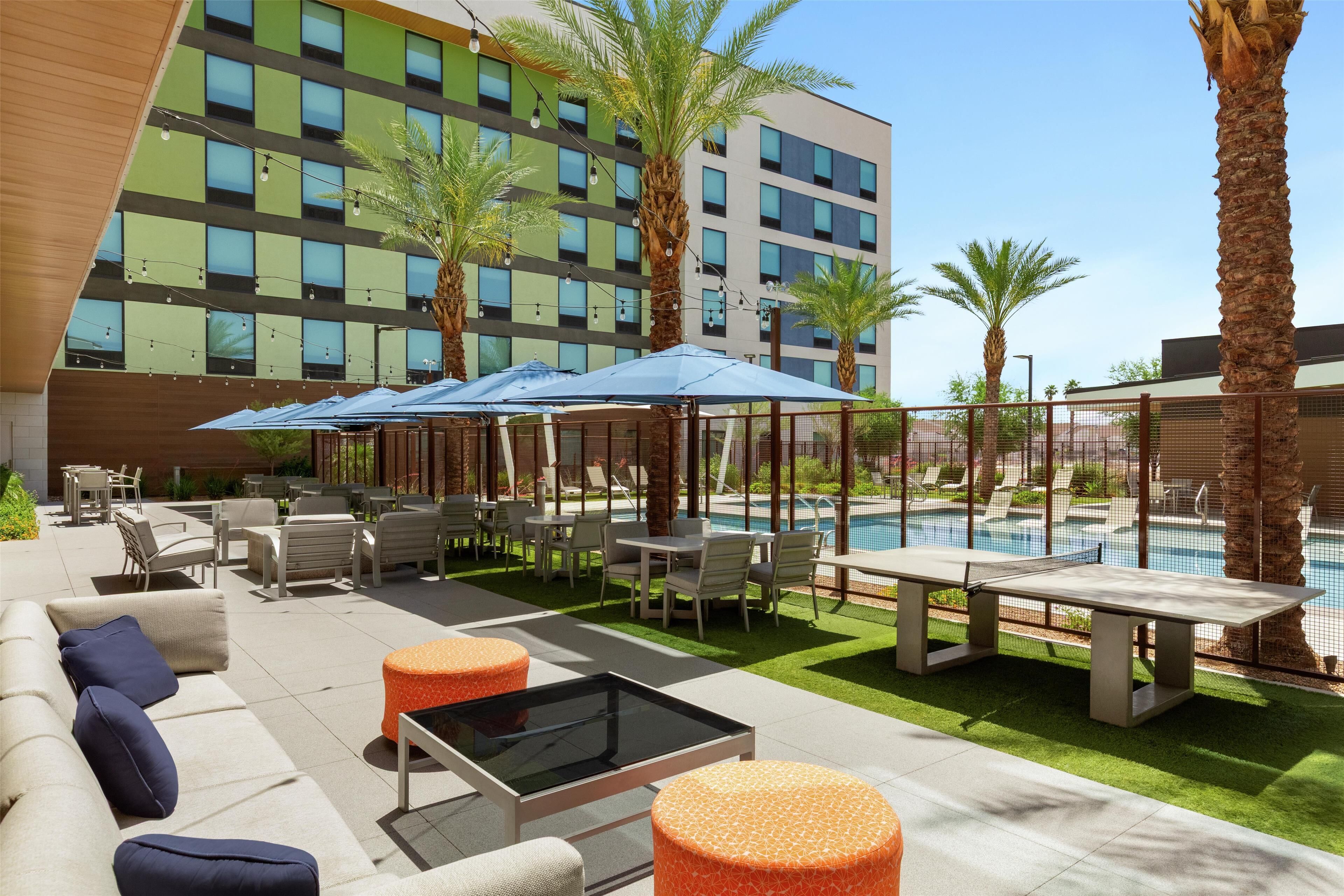 Eine Hotelterrasse mit Sitzgelegenheiten im Freien, einem Pool und Palmen.
