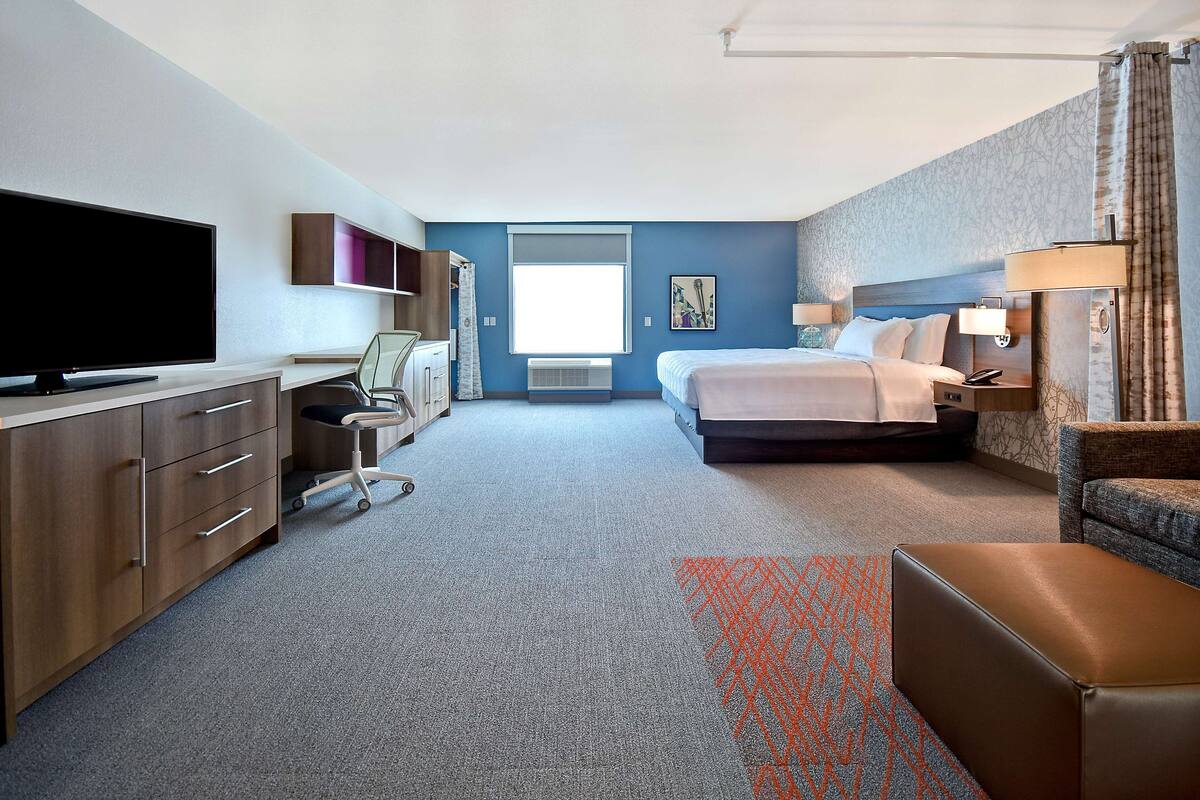 Hotelkamer met een bed, een bureau met een flatscreen televisie, een stoel, een bureaulamp en een raam.