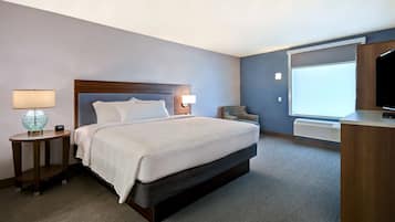Une chambre d’hôtel comprenant un lit, une table de chevet avec une lampe, une chaise, un bureau avec une télévision et une grande fenêtre.
