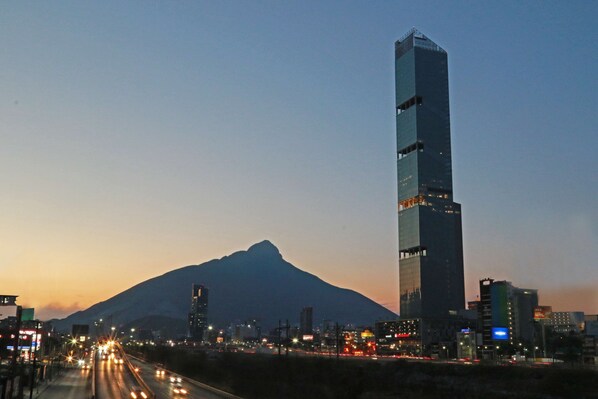 A tall skyscraper with a unique design, surrounded by a cityscape and a mountain in the background. - Hilton Garden Inn Monterrey Obispado (Monterrey)