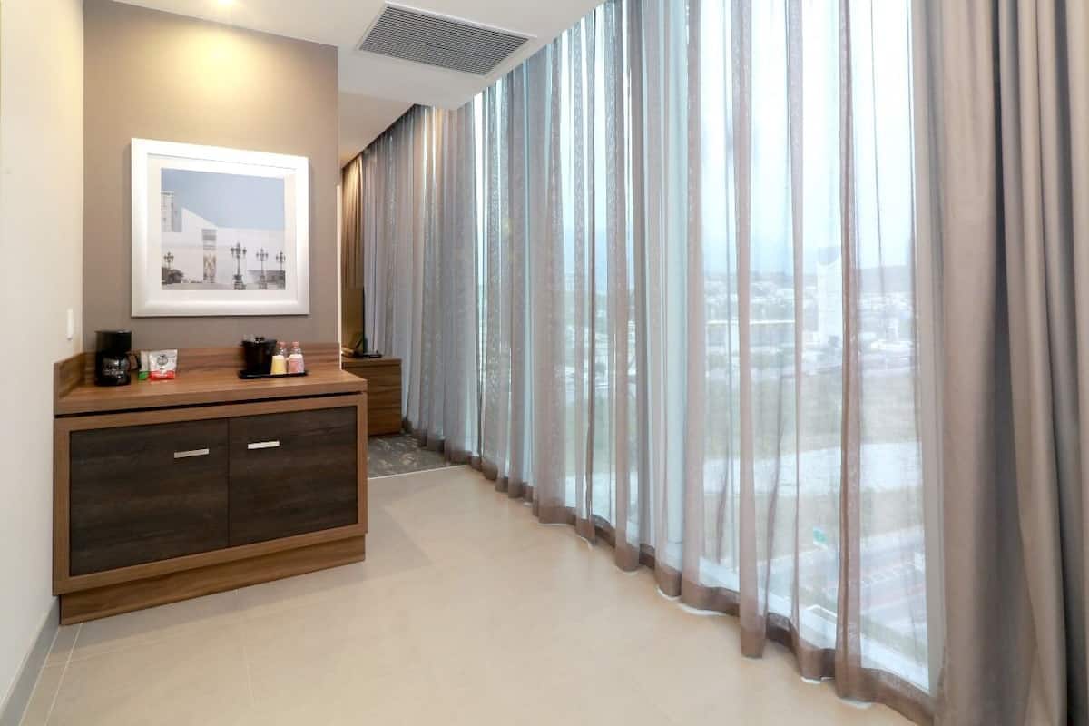 Ein Hotelzimmer mit großem Fenster, einem Holzschrank und einem gerahmten Bild an der Wand.