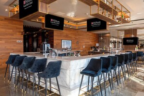 A modern bar area with a long counter, multiple bar stools, and overhead signage for Hilton Garden Inn Monterrey Obispado. - Hilton Garden Inn Monterrey Obispado (Monterrey)