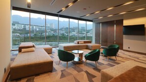 A modern hotel room with large windows, a city view, and a seating area with green chairs and a round table. - Hilton Garden Inn Monterrey Obispado (Monterrey)