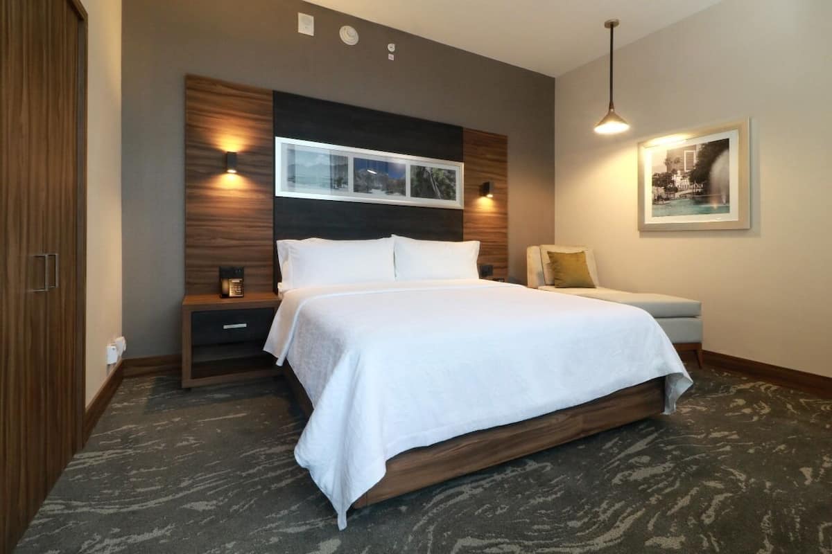 A modern bedroom with a large bed, a nightstand, a bedside table, and a wall-mounted light fixture.