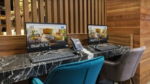 Two computer monitors displaying hotel room layouts, a telephone, and a keyboard on a marble countertop with teal and gray chairs. - Hilton Garden Inn Monterrey Obispado (Monterrey)