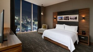 A modern hotel room with a large bed, a desk, a chair, and a city view. - Hilton Garden Inn Monterrey Obispado (Monterrey)