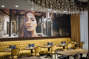 A restaurant with a yellow upholstered sofa, wooden tables, and chairs.