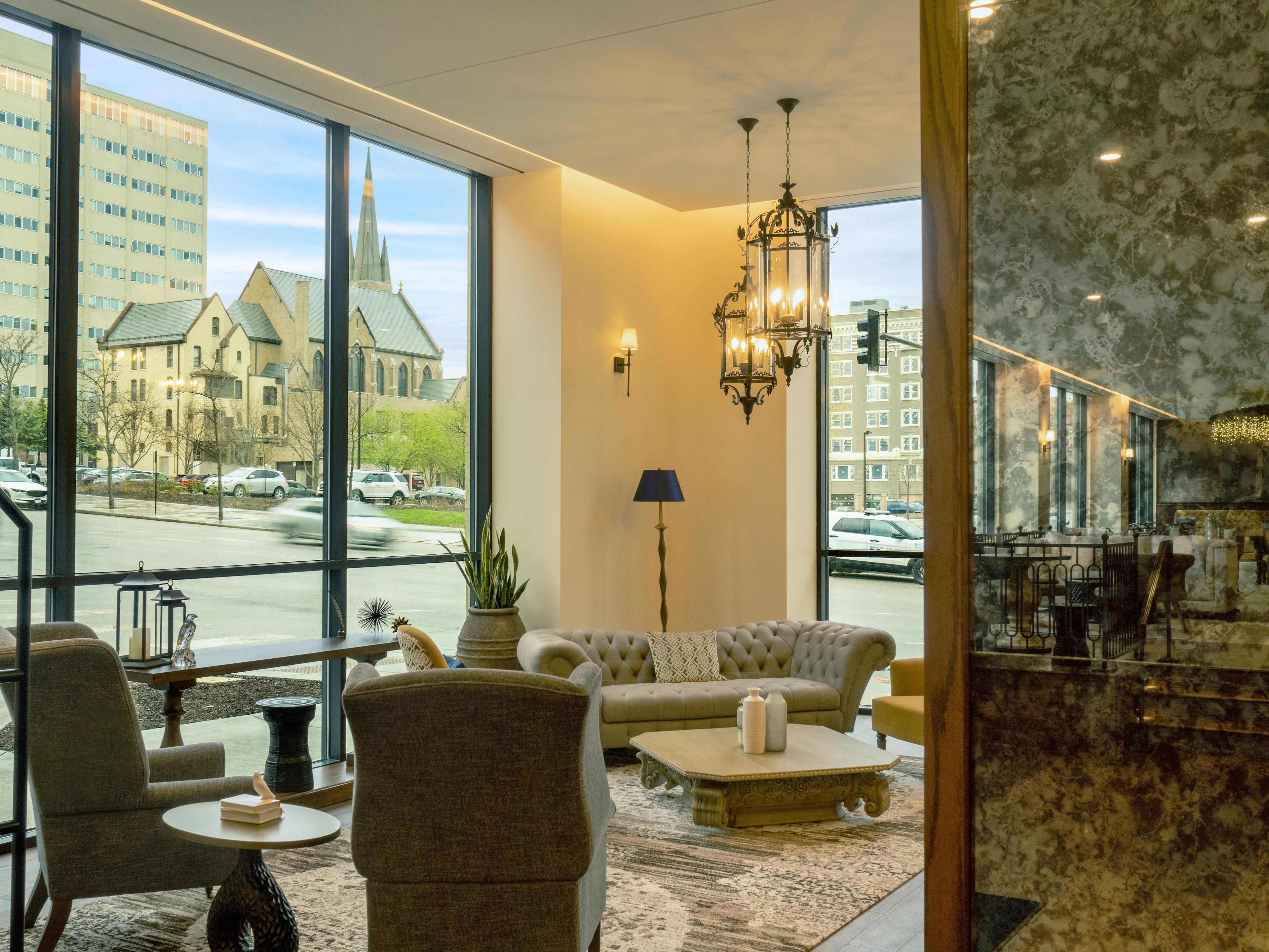 A hotel lobby with a large window, a chandelier, and a seating area with a sofa and armchairs.