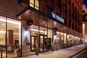 A hotel entrance with glass doors, a sign reading "THE PEREGRINE," and large potted plants on the sidewalk. - The Peregrine Omaha Downtown, Curio Collection by Hilton (Omaha)