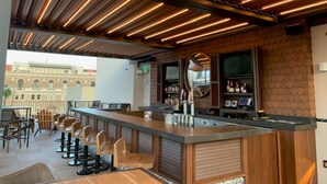 A bar area with wooden ceiling slats, a counter with stools, and a view of a building outside.