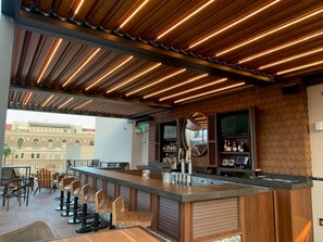 A bar area with wooden ceiling slats, a counter with stools, and a view of a building outside. - The Peregrine Omaha Downtown, Curio Collection by Hilton (Omaha)