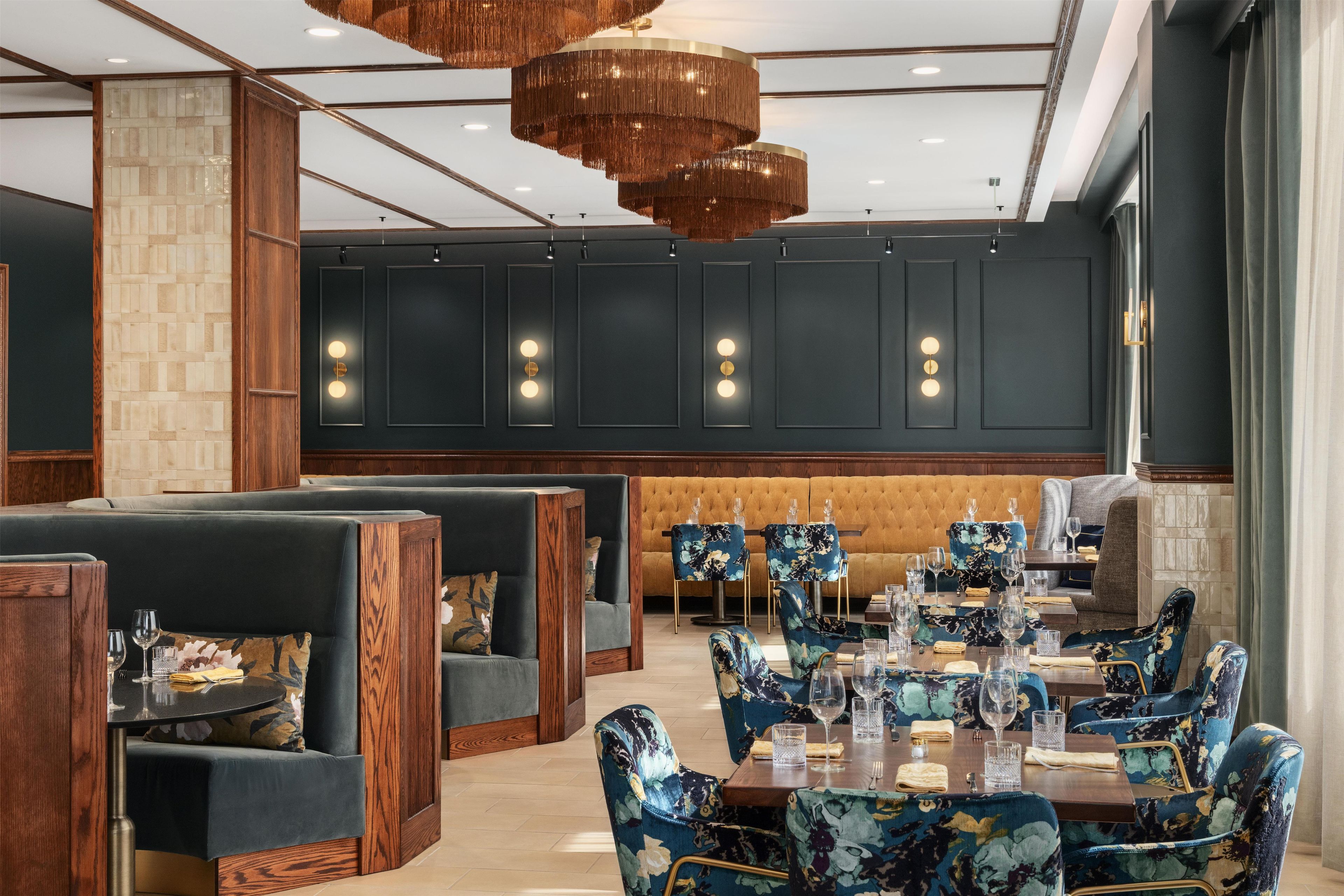 A restaurant interior with booths, a long dining table, and hanging chandeliers.