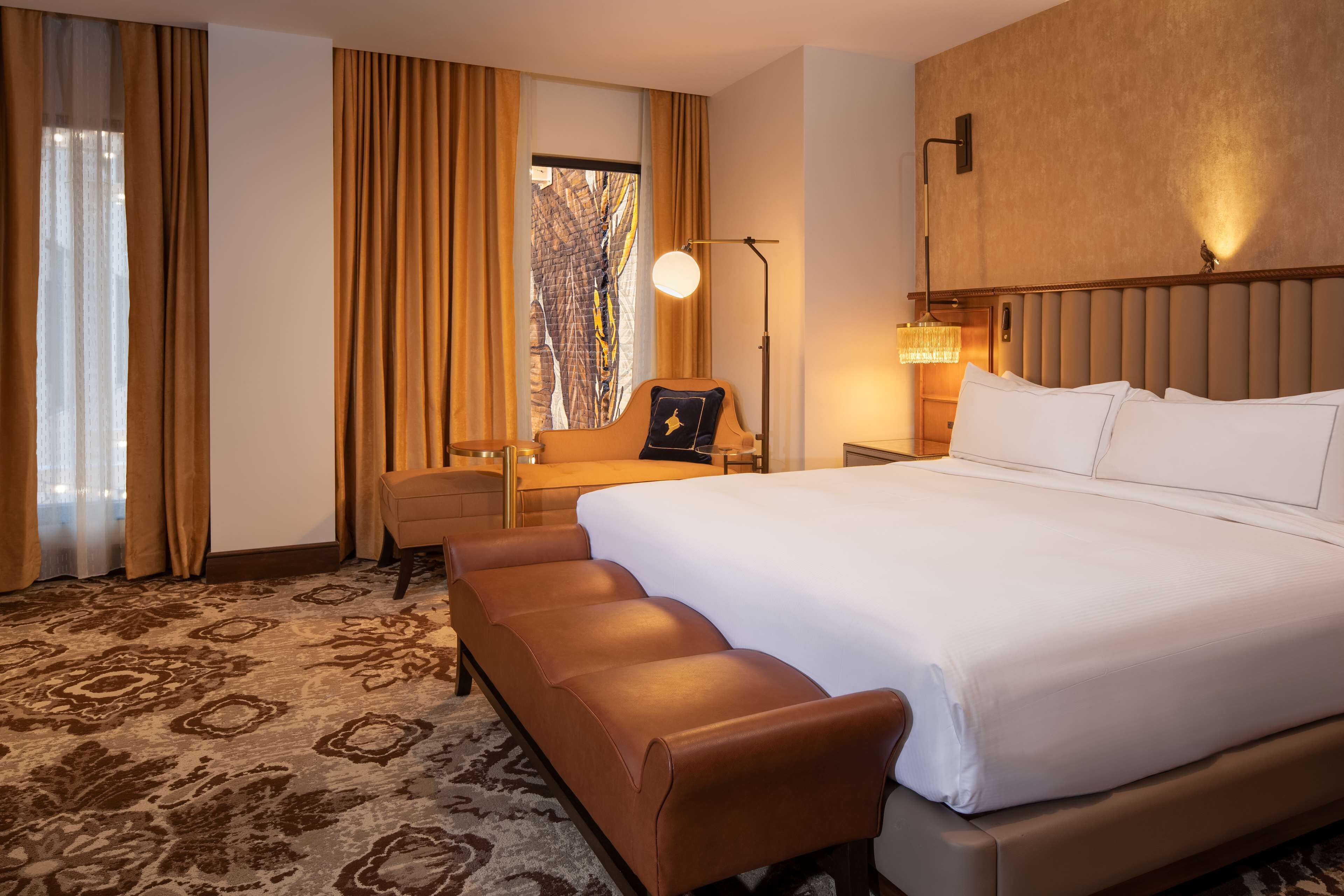 A hotel room with a large bed, a sofa, a desk, and a view of trees through the window.