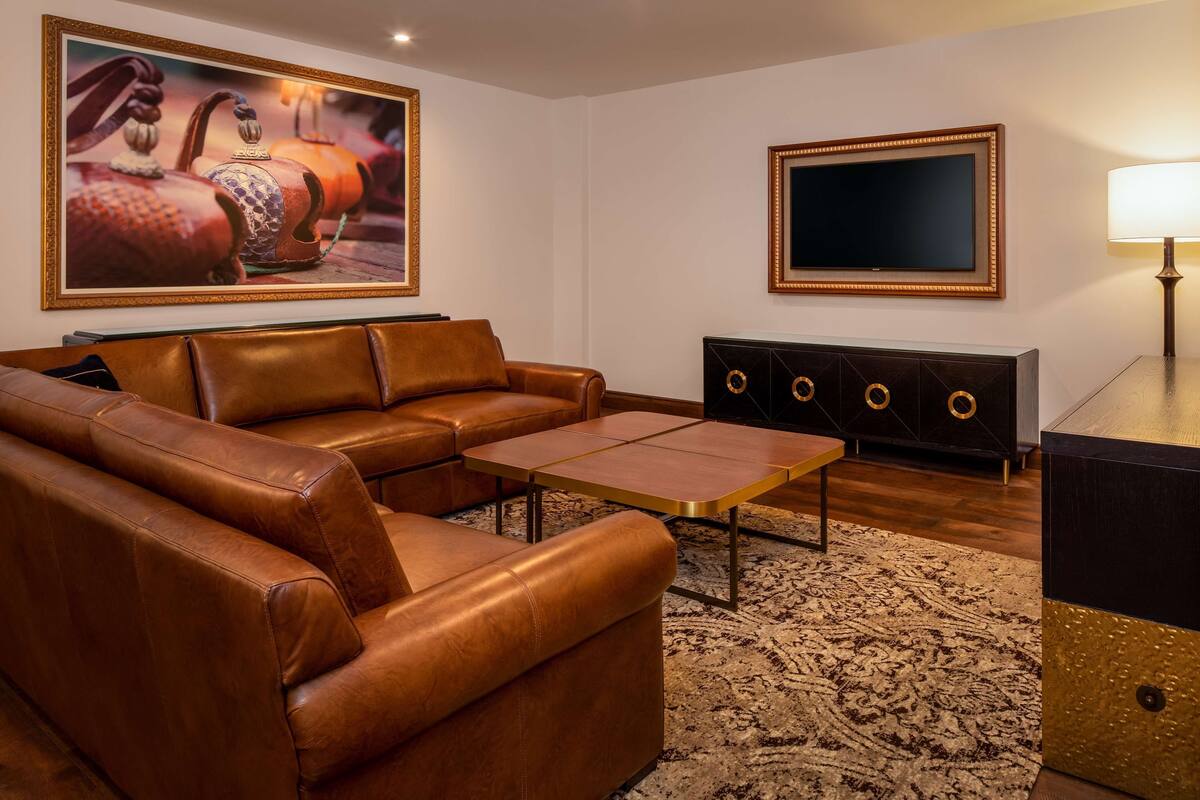 A living room with a brown leather sofa, a coffee table, a black entertainment unit with gold accents, and a large framed picture on the wall.