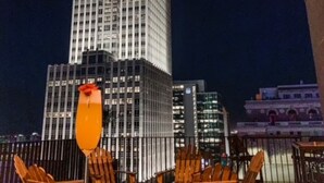 An outdoor seating area with wooden chairs and a table, a fire pit, and a glass of orange beverage.