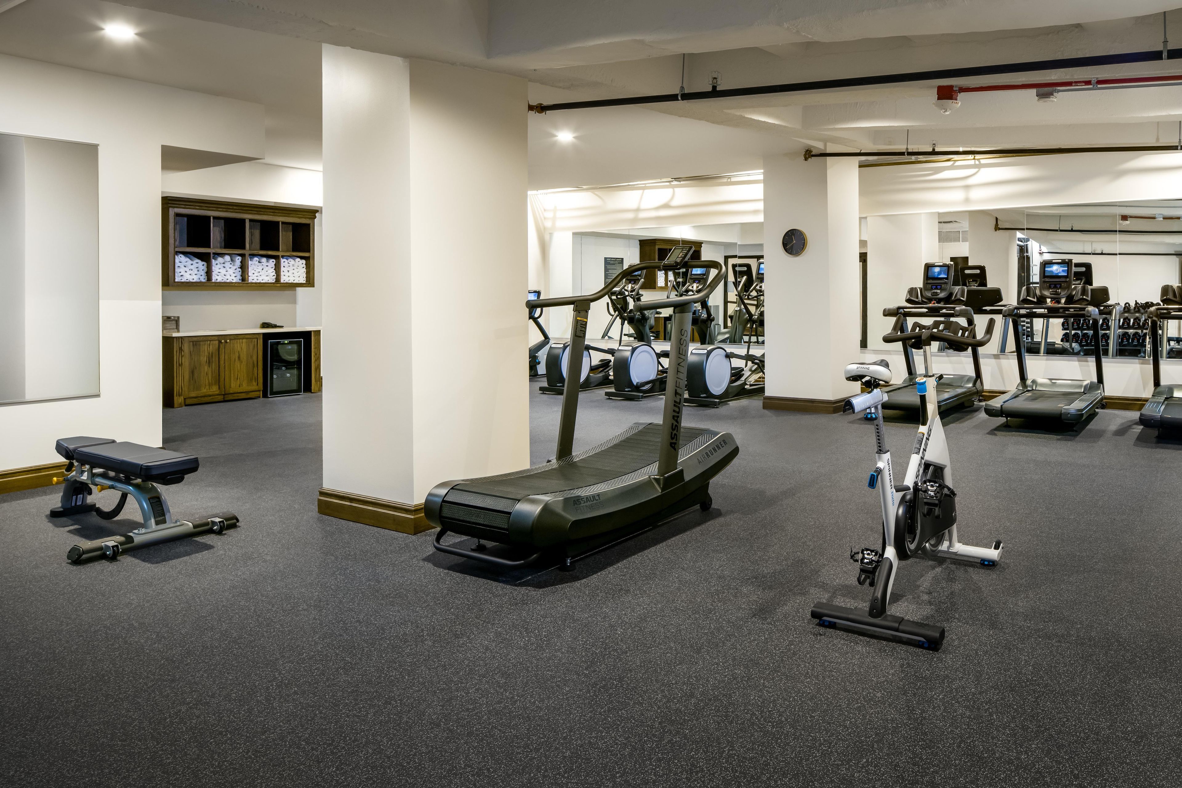 Et fitnessrum med løbebånd, motionscykler og en bænk.