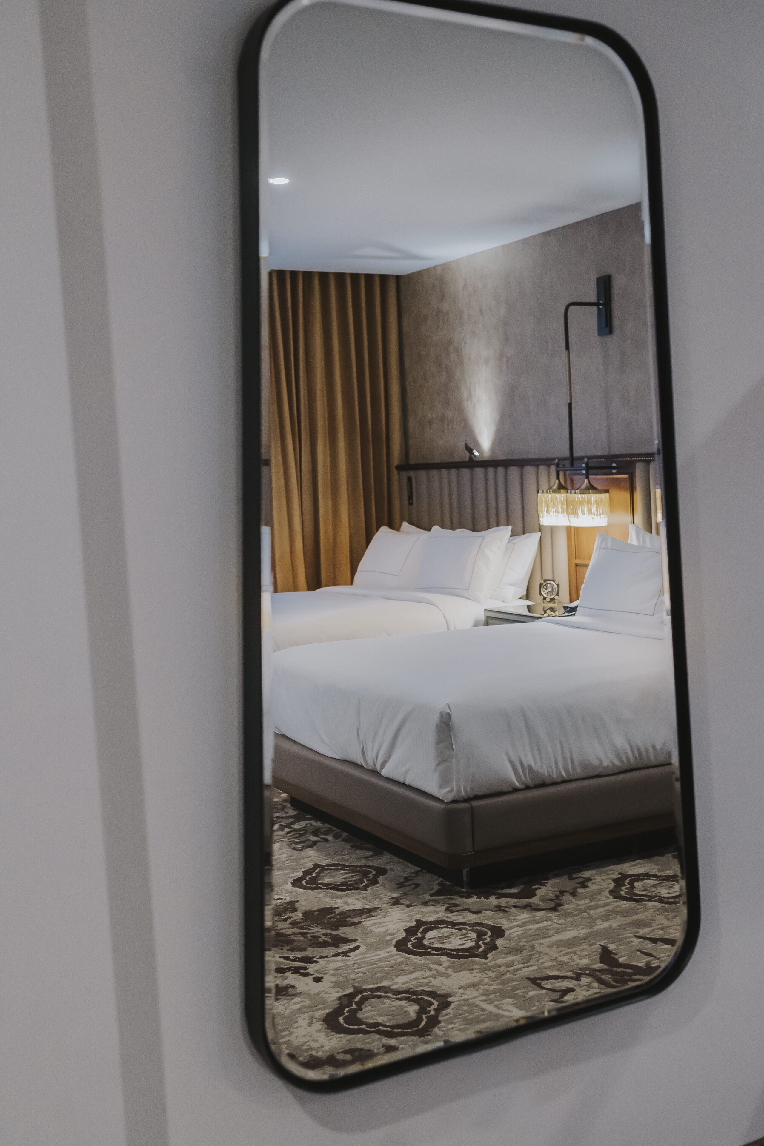 A hotel room with a large bed, a nightstand, a lamp, and a mirror.