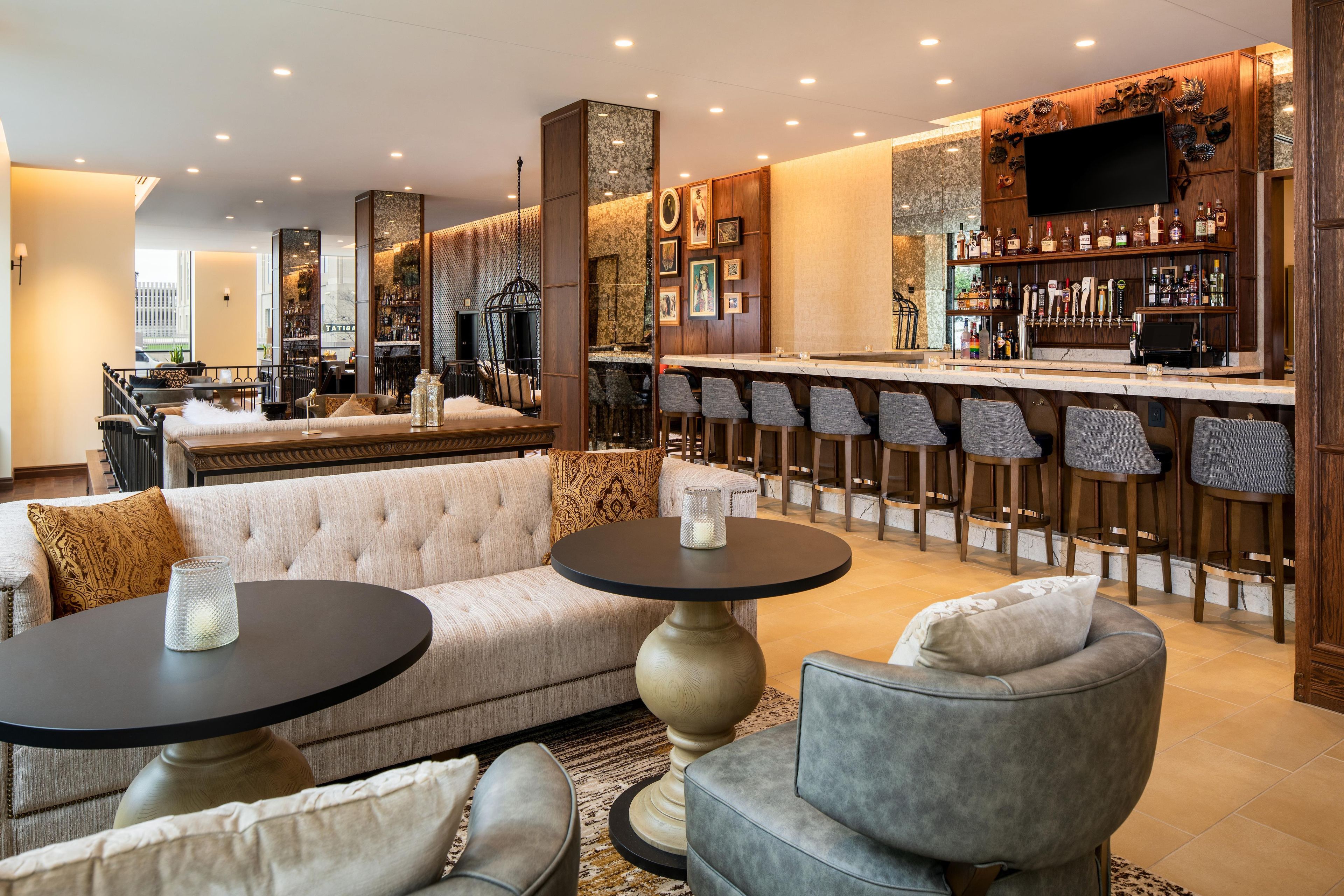 A bar area with a long counter, multiple stools, and a variety of bottles.
