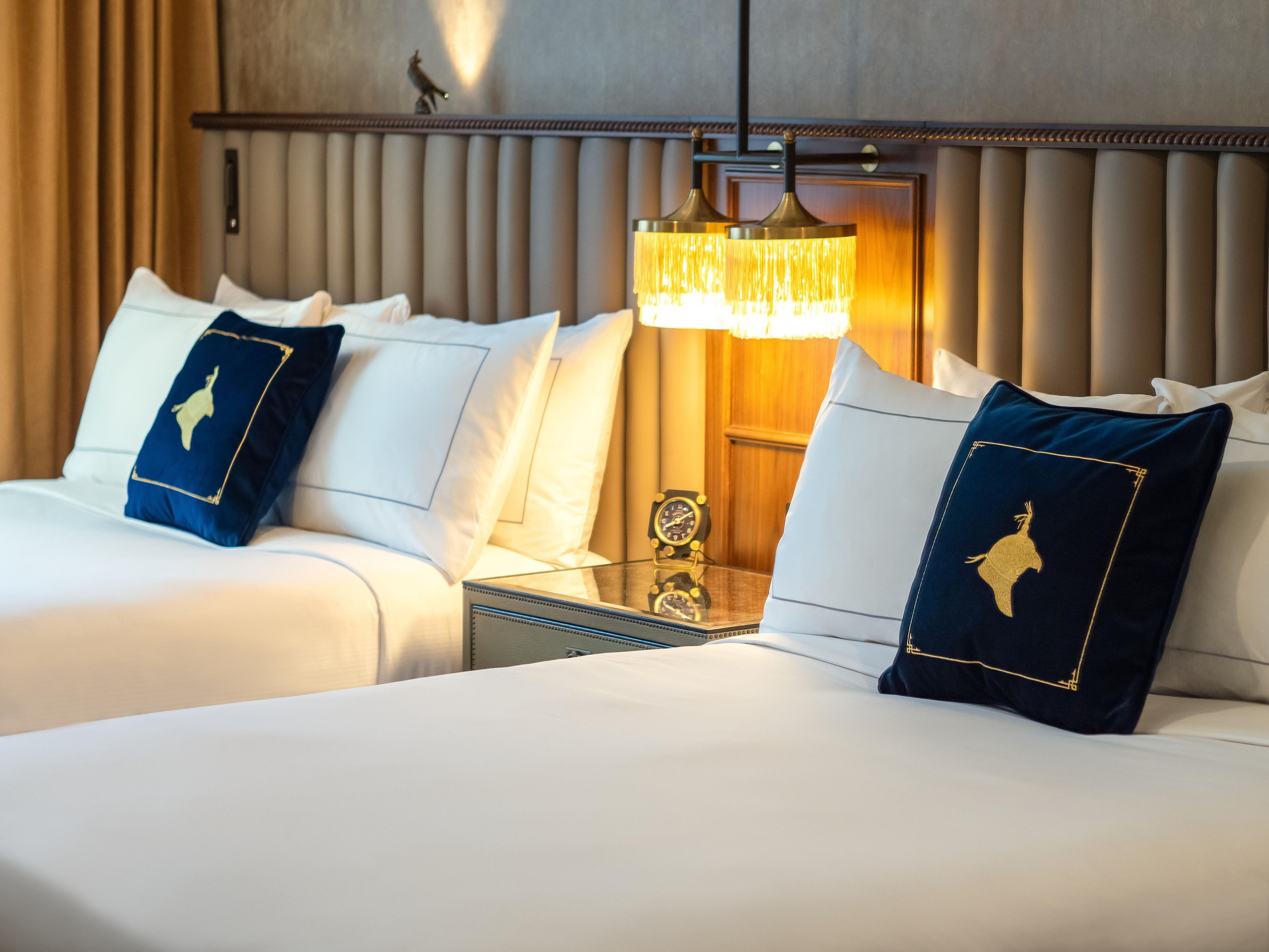 Une chambre d’hôtel avec deux lits, une table de chevet avec une horloge et une lampe fixée au mur.