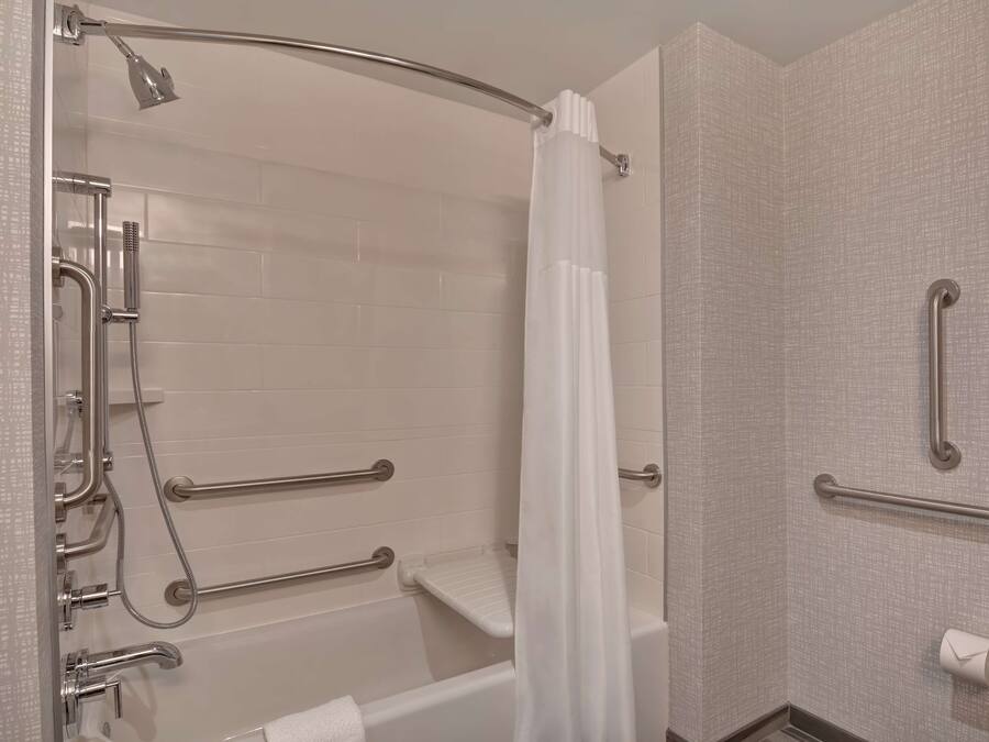 Un baño moderno con ducha a ras de suelo, barras de apoyo, cortina de ducha blanca y dispensador de papel higiénico.