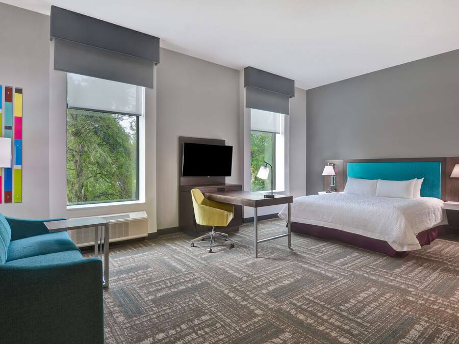 A modern hotel room with a large bed, a desk, a chair, and a TV.
