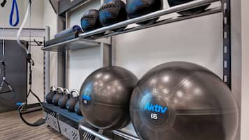 Un gimnasio con equipamiento de ejercicio, incluyendo balones medicinales y una máquina de poleas.